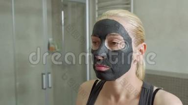 那个女人把泥面罩戴在脸上。 你的面部护理。 泥浆水疗程序。 日间水疗中心。 在人身上画一个黑色面具